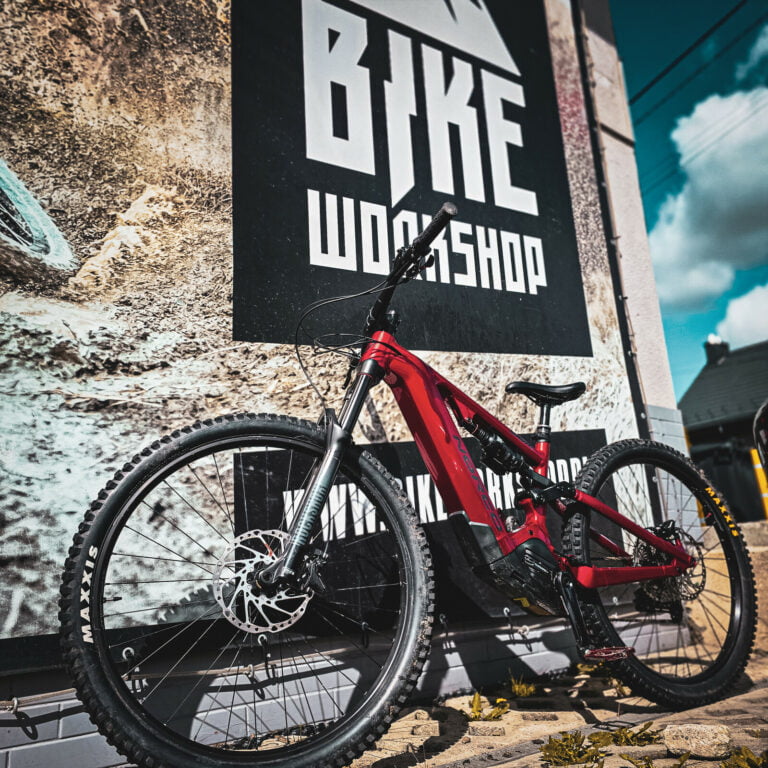 Czerwony elektryczny rower enduro przed banerem BikeWorkshop w Bielsku-Białej